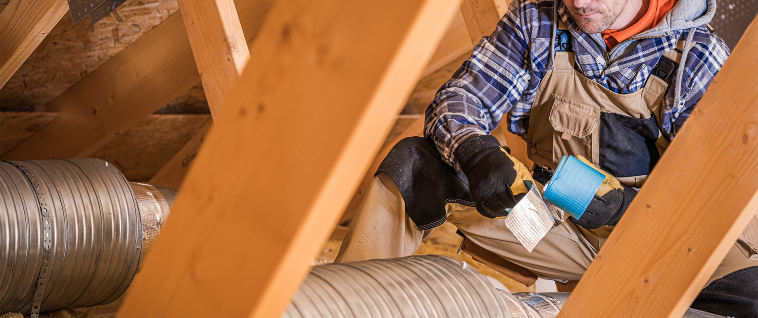 Man Holding Ducttape Working On Ducts In Attic