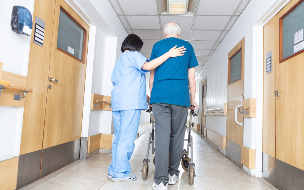 Caretaker Helping Elderly Man Walk To Room